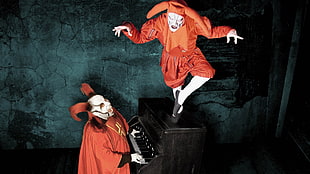 two jester in orange costume playing a black piano