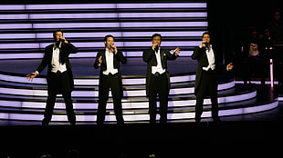 four men wearing black-and-white suits standing on stage
