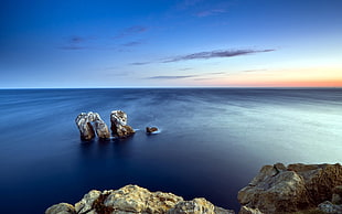 photography of arch-shaped rock on body of water during golden hour