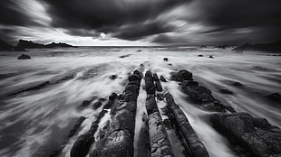 grayscale photo of rock formations covered with clouds, rocks, water