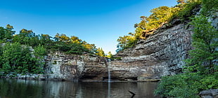 photo of running water surround by trees and rock under blue calm sky