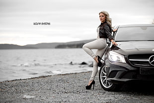 woman in white jeans leaning on black car
