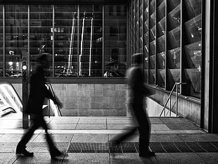 grayscale photo of two human walking near stairs