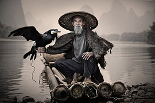 man in grey shirt and black pants sitting with black bird