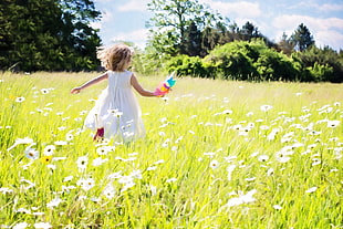 girl in white sleeveless dress running on green grass field full of white flowers during daytime