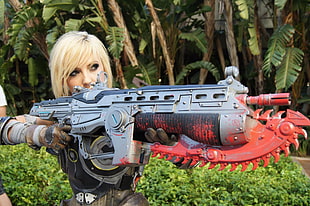 photo of woman with blonde hair wearing cosplay costume holding gun during day time