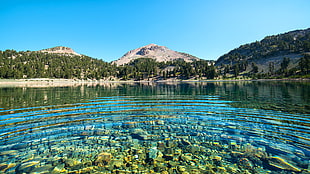 body of water near mountains under blue and white sunny sky during daytime