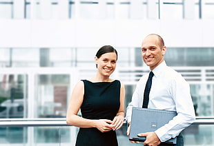 man in white dress shirt carrying laptop while standing beside woman in black dress