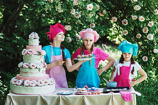 three woman wearing aprons standing in front 3-tier floral cake