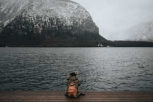 human wearing a brown backpack sitting on edge of lake port