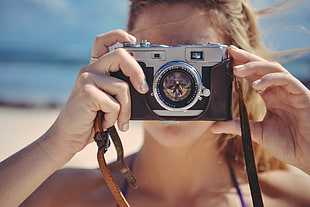 woman holding silver DSLR camera while taking photo during daytime