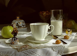 ceramic cup on saucer near highball glass filled with milk near spoon