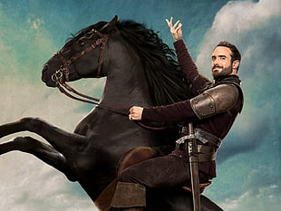 man riding black horse with blue clouds in background