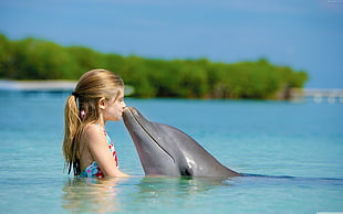 blonde haired girl kissing dolphin on body of water