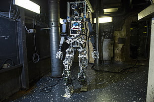 gray robot standing near black machine