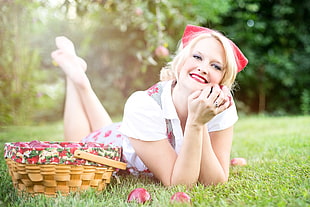 photo of a woman lying on grass field near wicker picnic basket