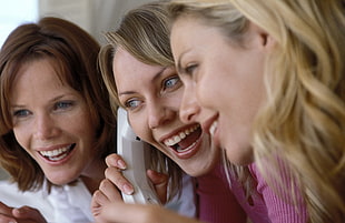 three woman smiling while holding the phone