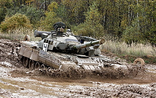 brown and green camouflage battle tank passing mud beside trees during daytime