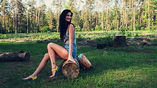 woman wearing gray sleeveless shirt sitting on wood log near forest