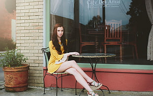 sitting woman wearing yellow long-sleeved dress in front of cafe