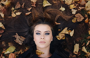 closeup photo of woman wearing black top lying on brown surface beside leaves
