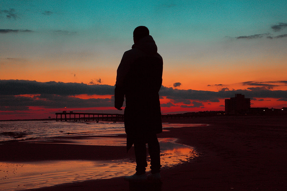 silhouette of man wearing coat near ocean shore HD wallpaper