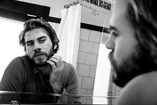 grayscale photo of man checking his beard on mirror