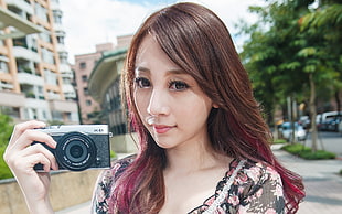 woman in black white and pink floral scoop-neck shirt holding black and silver camera during daytime
