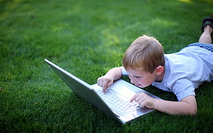 boy lying on grass while typing laptop computer
