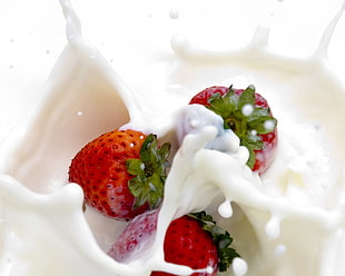 three red strawberries covered with white milk