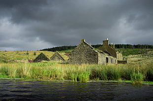 house surrounded by green grass near lake during dark clouds days