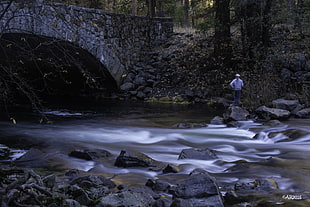 man standing in the rock near the bridge and river, merced river