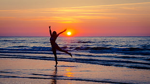 silhouette of woman dancing near seawave during sunset