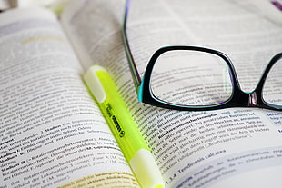black framed eyeglasses with green marker on book page
