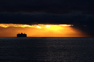 silhouette of ship on body of water during sunset