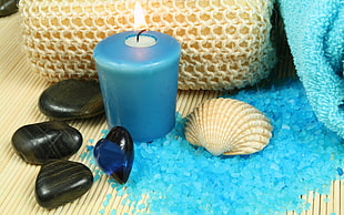 four black pebbles beside blue candle and white sea shell