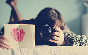 woman holding camera and hook with red heart sketch on white bed focus photo