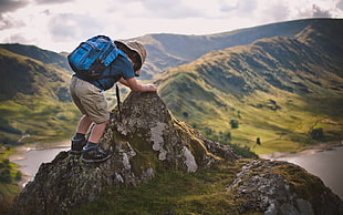 boy wearing blue shirt and brown shorts carrying blue backpack climbing on mountain