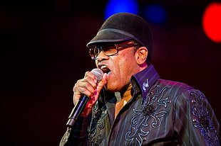 man wearing black collared button up shirt and black cap holding microphone