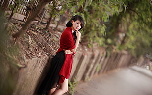 woman in red dress leaning on wall near trees