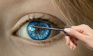 person holding black skeleton key with human's left eye background