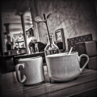 grayscale photo of ceramic mugs on wooden surface