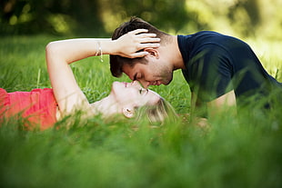 man in blue shirt on top of woman in pink laying on green grass field