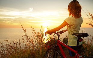woman in white cap-sleeved shirt holding red mountain bike under golden hour