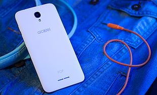white Alcatel smartphone beside orange audio cable