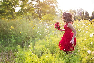 girl in red tank dress holding red flower running on flower field during daytime HD wallpaper