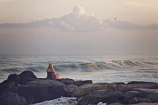 woman sitting on rock beside body of water