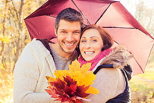 man and woman takes picture together under red umbrella during daytime