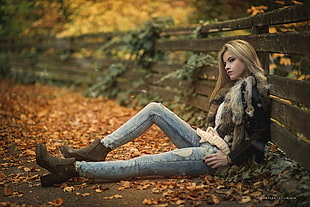 woman wearing black and brown fur jacket and blue distressed jeans leaning on brown wooden fences