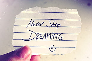 person holding white lined paper with text of never stop dreaming